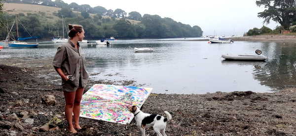 Joyful painting at Mylor Creek, down from the studio at Restronguet Barton, artist Chloë Tinsley stands looking out at the painting, the water and the dog looks at her, Cornish Artist
